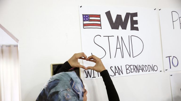A Muslim woman raises her hands in the shape of a heart to a sign that reads "We stand with San Bernardino."