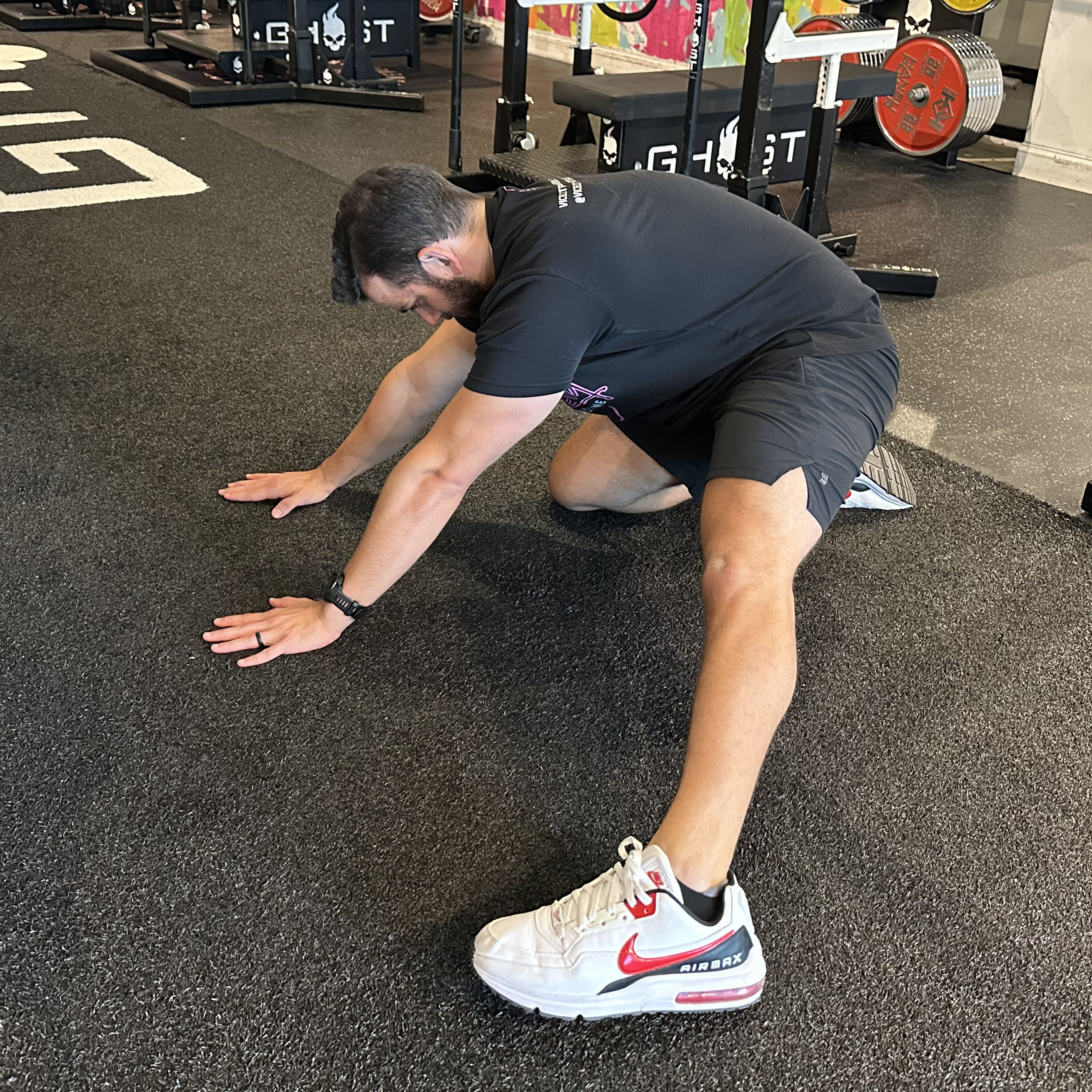A Vice City Sports Medicine performs and adductor rockback in a gym setting. He is on his hands and right knee, with his left leg positioned straight out to the side. 