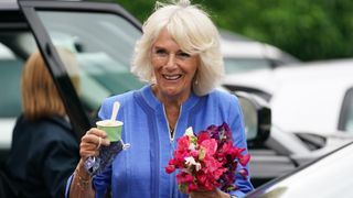 Queen Camilla holds a bunch of flowers and a small tub of ice cream during a visit to meet with the organisers of the Hay Festival in 2021