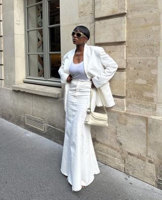 Loïcka Grâce wearing a white top, white blazer, and white fishtail skirt with brown sunglasses.