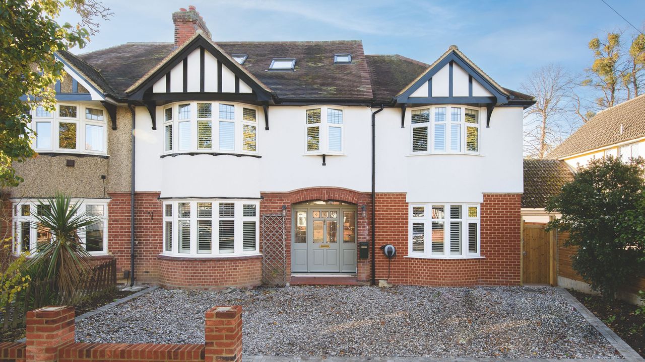 Exterior of a semi-detached house, with brickwork at the bottom at white render at the top of the house, and a gravel driveway