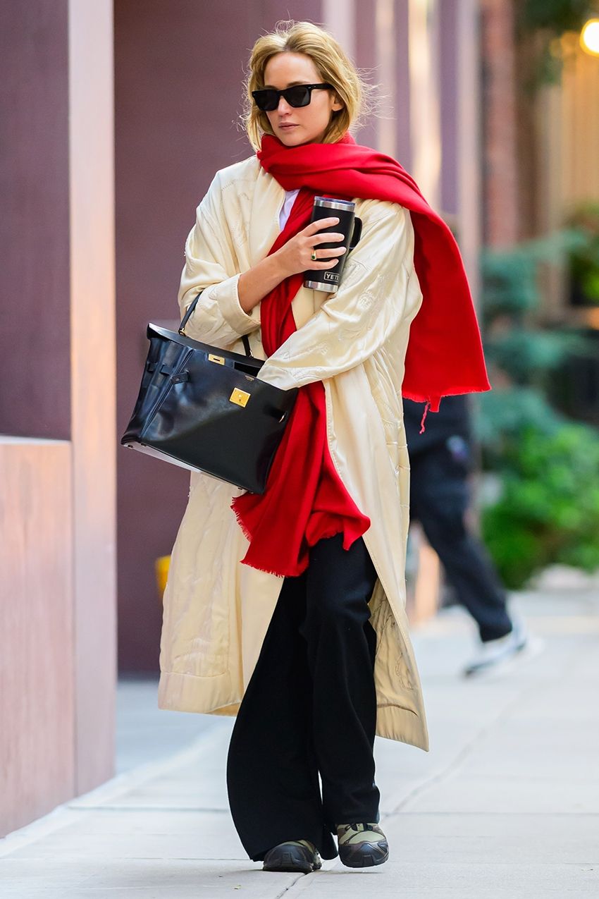 Jennifer Lawrence wearing a cream coat, red scarf, black pants, sneakers, and a Hermès Birkin bag in NYC