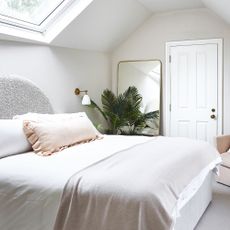 A white loft bedroom with a large mirror leaning against the wall and a plant