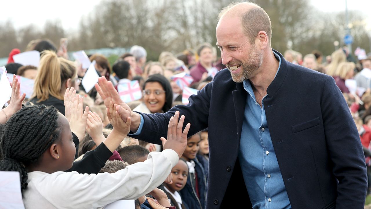 Prince William wearing a blue shirt and jacket giving a high five to a boy in a crowd of fans in March 2025