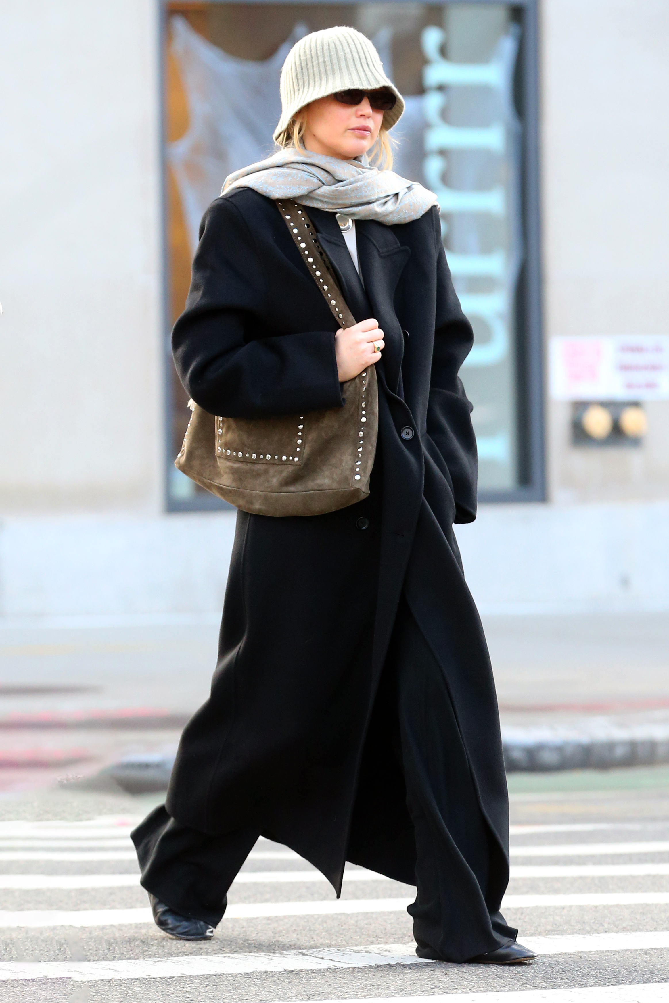 Jennifer Lawrence is pictured in New York wearing an outfit inspired by a 90s romcom in a knit hat, grey scarf, studded suede bag and oversized trench coat.