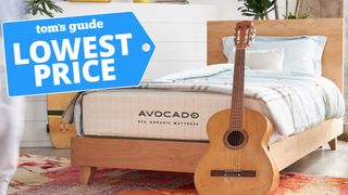 Image shows the Avocado Eco Organic Mattress on a wooden frame with an acoustic guitar leaning against the base