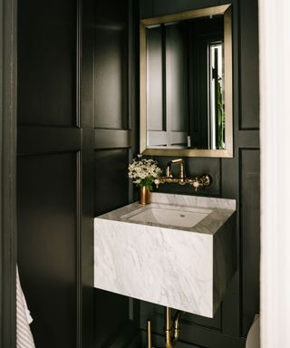 Black panel walls, gold taps, marble design sink