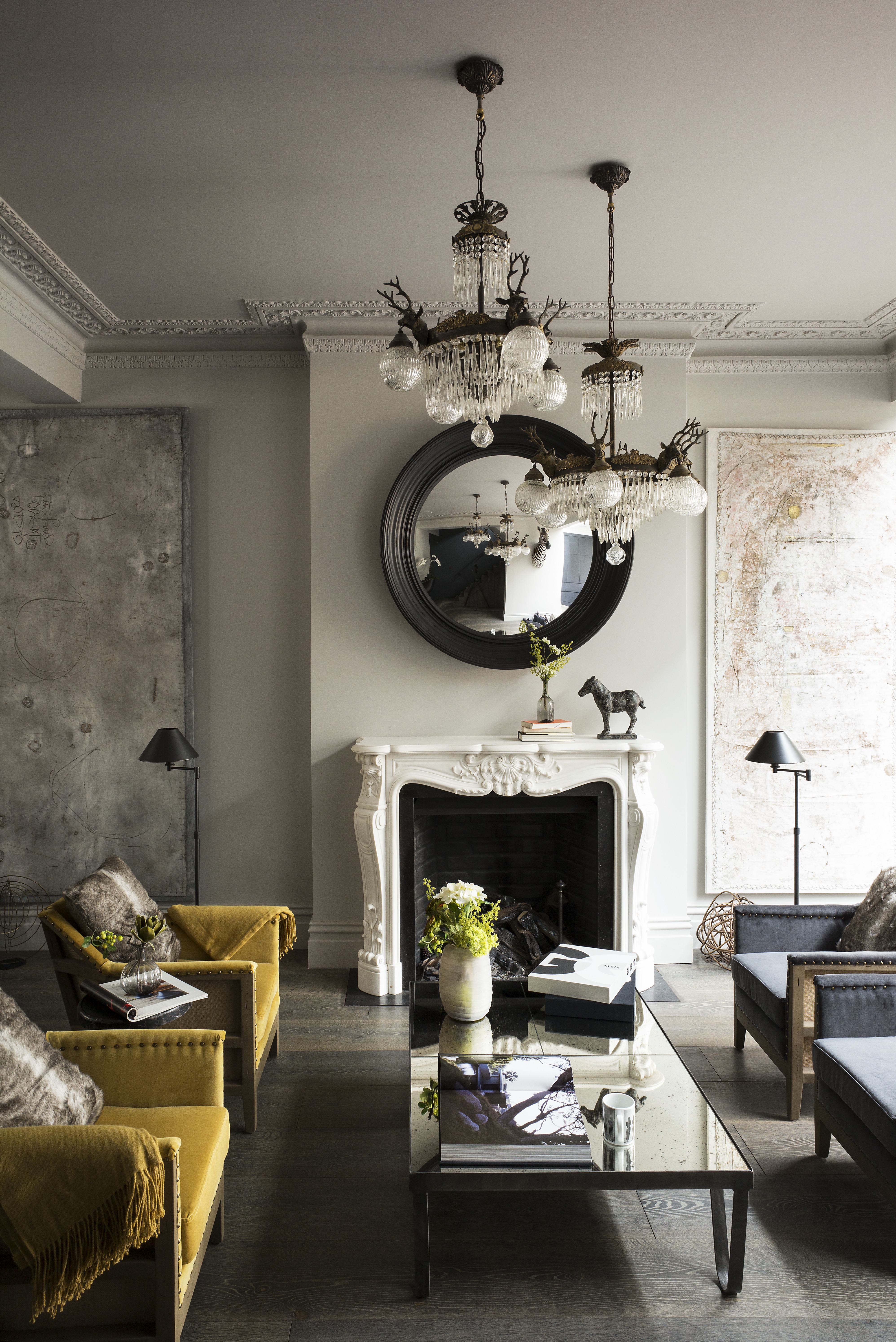 A yellow living room with velvet yellow chairs and a large white fireplace