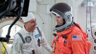 a man in a white suit smiles and laughs while talking to a man in an orange space suit who is preparing to board a space shuttle