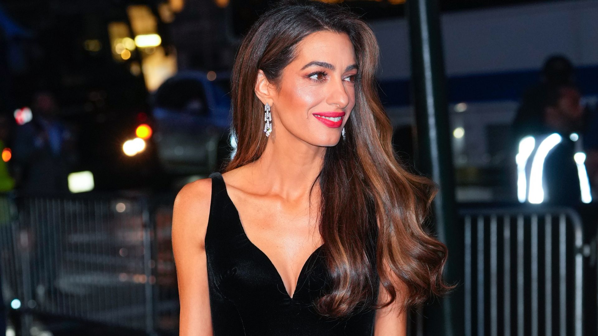 Amal Clooney is photographed wearing a long black velvet dress with diamond earrings.