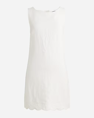 a white shift dress from jcrew with a scalloped hem in front of a plain backdrop