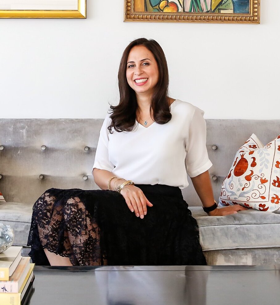 A photo of a woman with dark hair sat on a sofa smiling at the camera