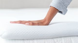 A hand touches the surface of the Perfectly Snug the Smart Topper cooling mattress topper to feel the temperature