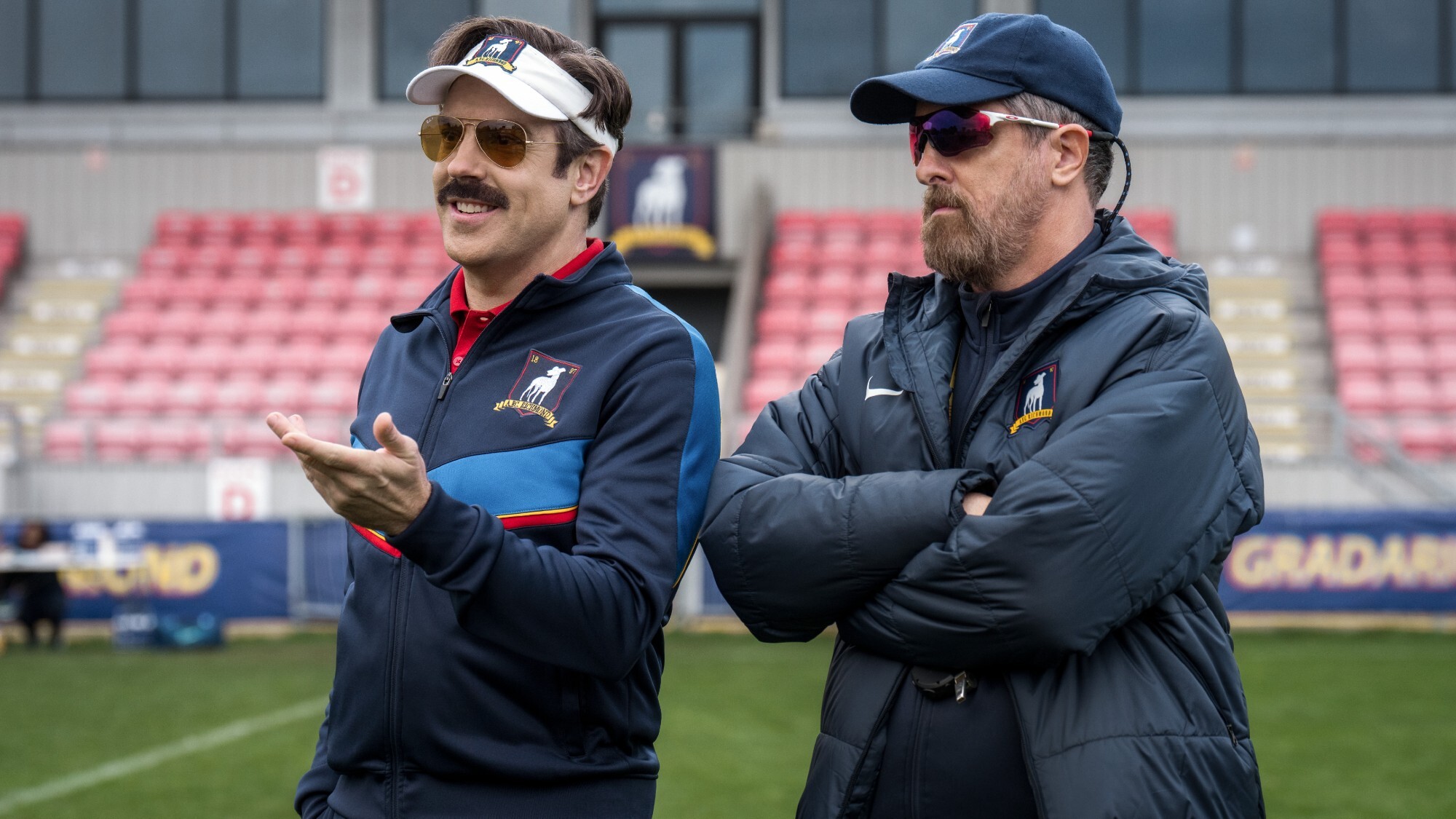 Jason Sudeikis as Ted Lasso standing next to Brendan Hunt as Coach Beard in Ted Lasso Season 4.