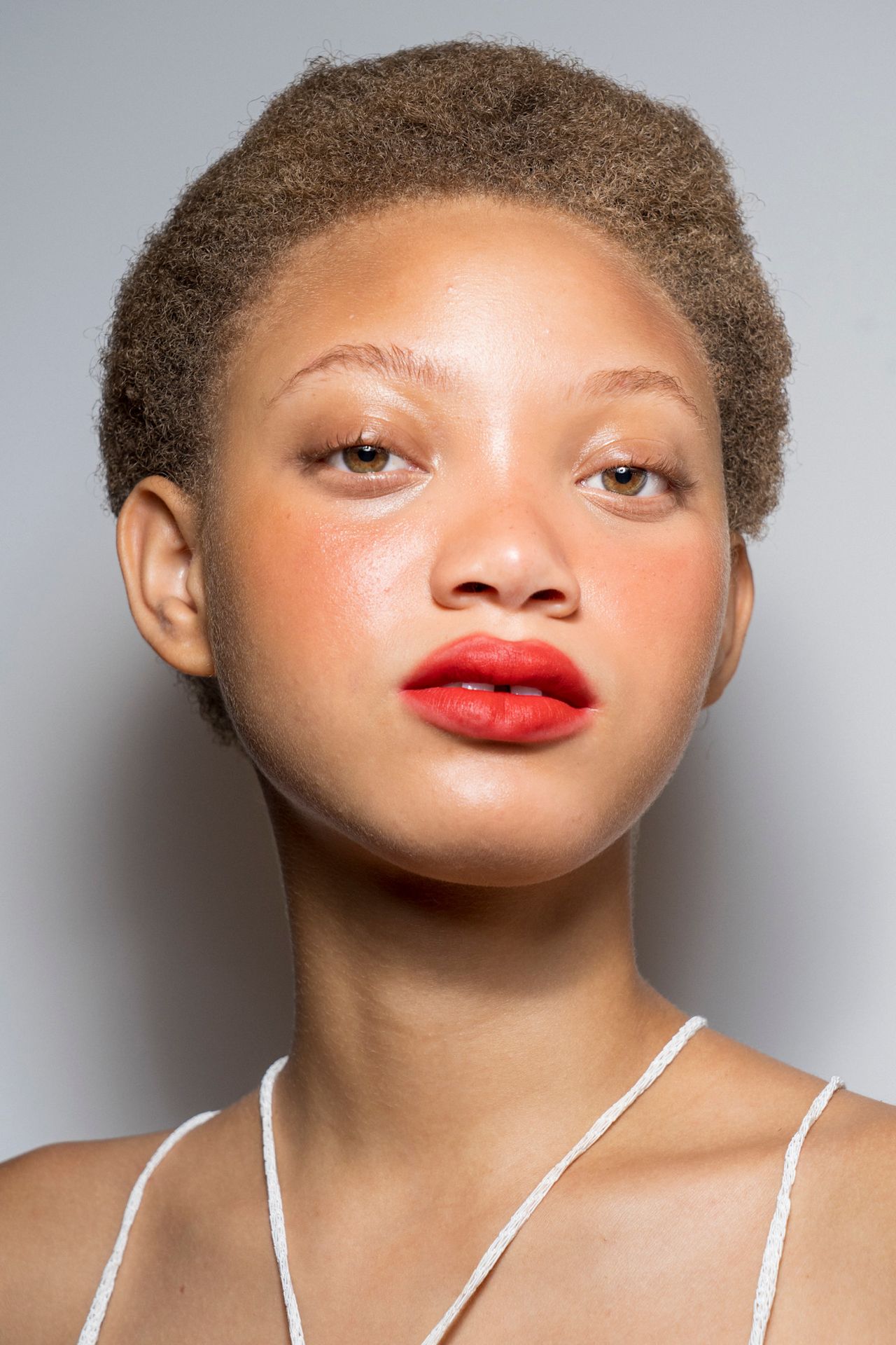 A red lip, glossy eye, and no mascara at Camps on a model in a white halter top