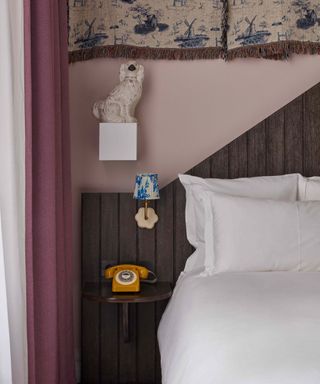 A light purple bedroom with a wooden bedframe, darker purple drapes, white sheets and a little yellow telephone