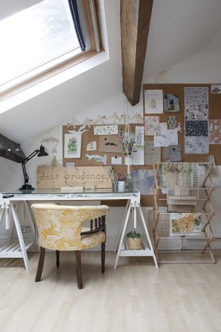White home office with cork pinboard, white desk, yellow and wood armchair and dryer stand used to dry prints