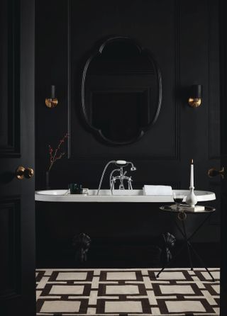 black and white bathroom with black tub, black and white graphic floor, wall lights, mirror