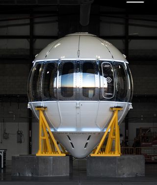 a metal orb-shaped capsule lined with windows in a hangar