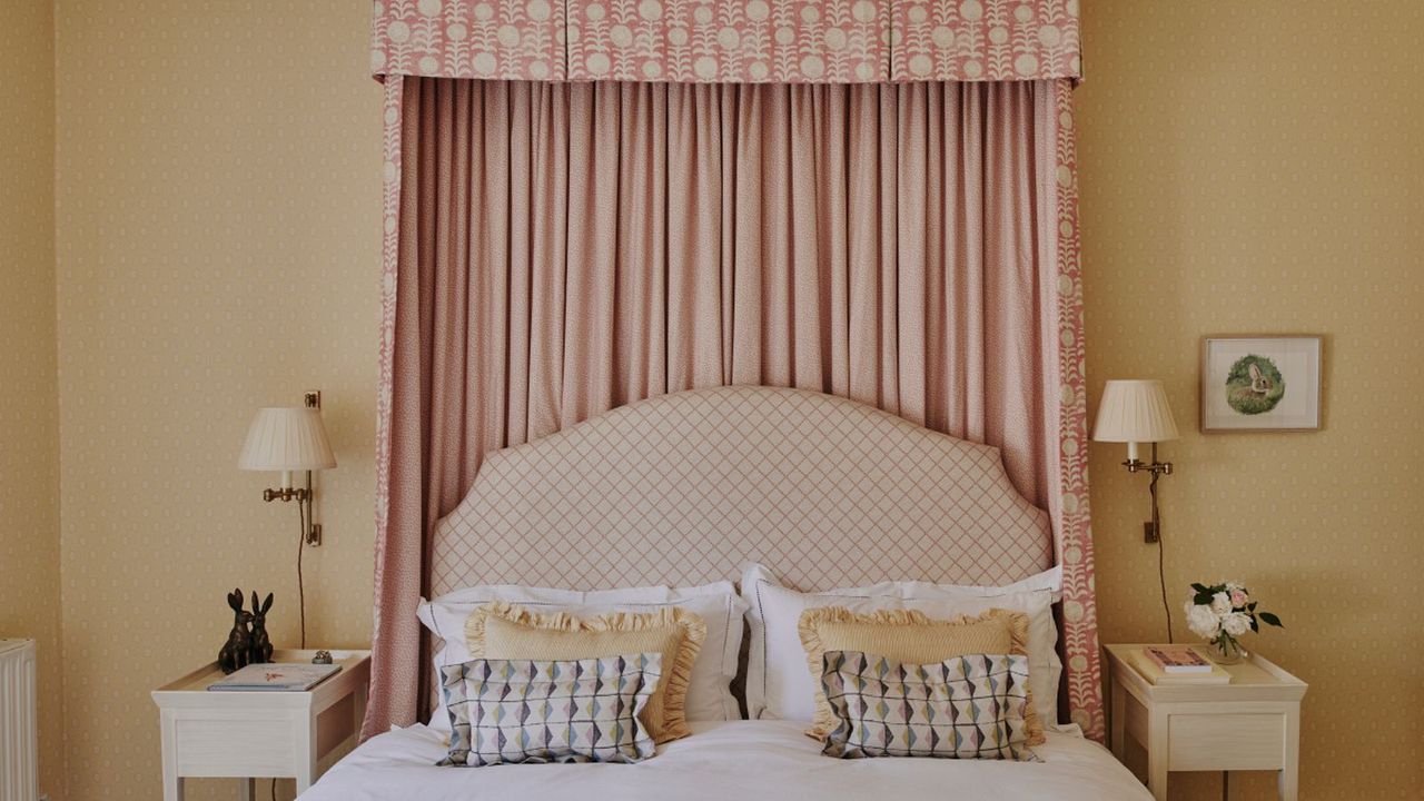 Spring bedroom with yellow pastel walls, bed canopy, printed headboard, wall sconces and yellow frilly cushions