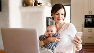 baby and mother in front of laptop holding a smartphone