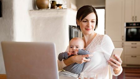 baby and mother in front of laptop holding a smartphone