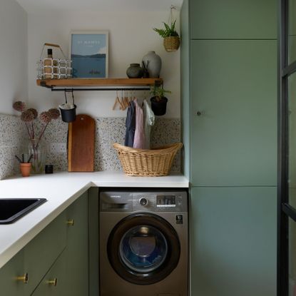 Grey washing machine in a kitchen with green cabinets and a white worktop