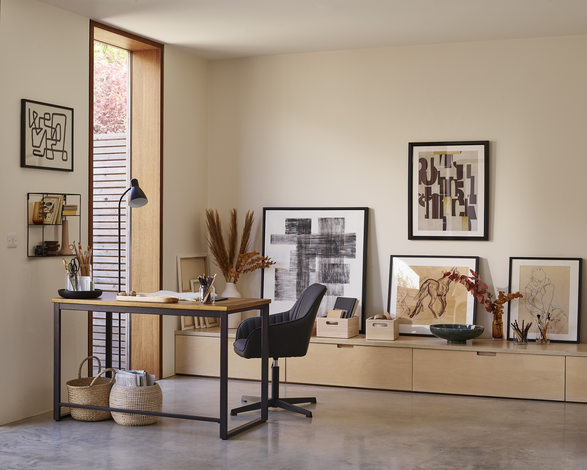 Brown, beige and black home office, with a gallery wall and low side table, and a wooden desk and black chair next to a floor-to-ceiling window