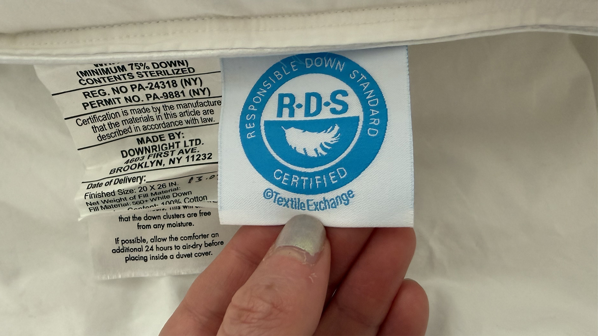 A close up of a hand holding a label on the Downright Mackenza WD pillow showing it has Responsible Down Standard Certification from the Textile Exchange