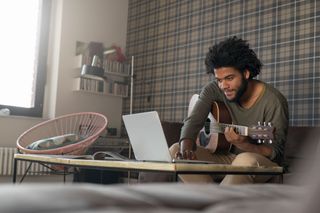 Man uses a laptop while playing acoustic guitar