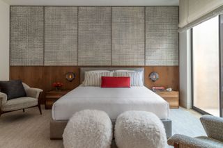 japandi bedroom with textured wall panels, extended timber headboard, armchair, fluffy ottoman and low-slung bed