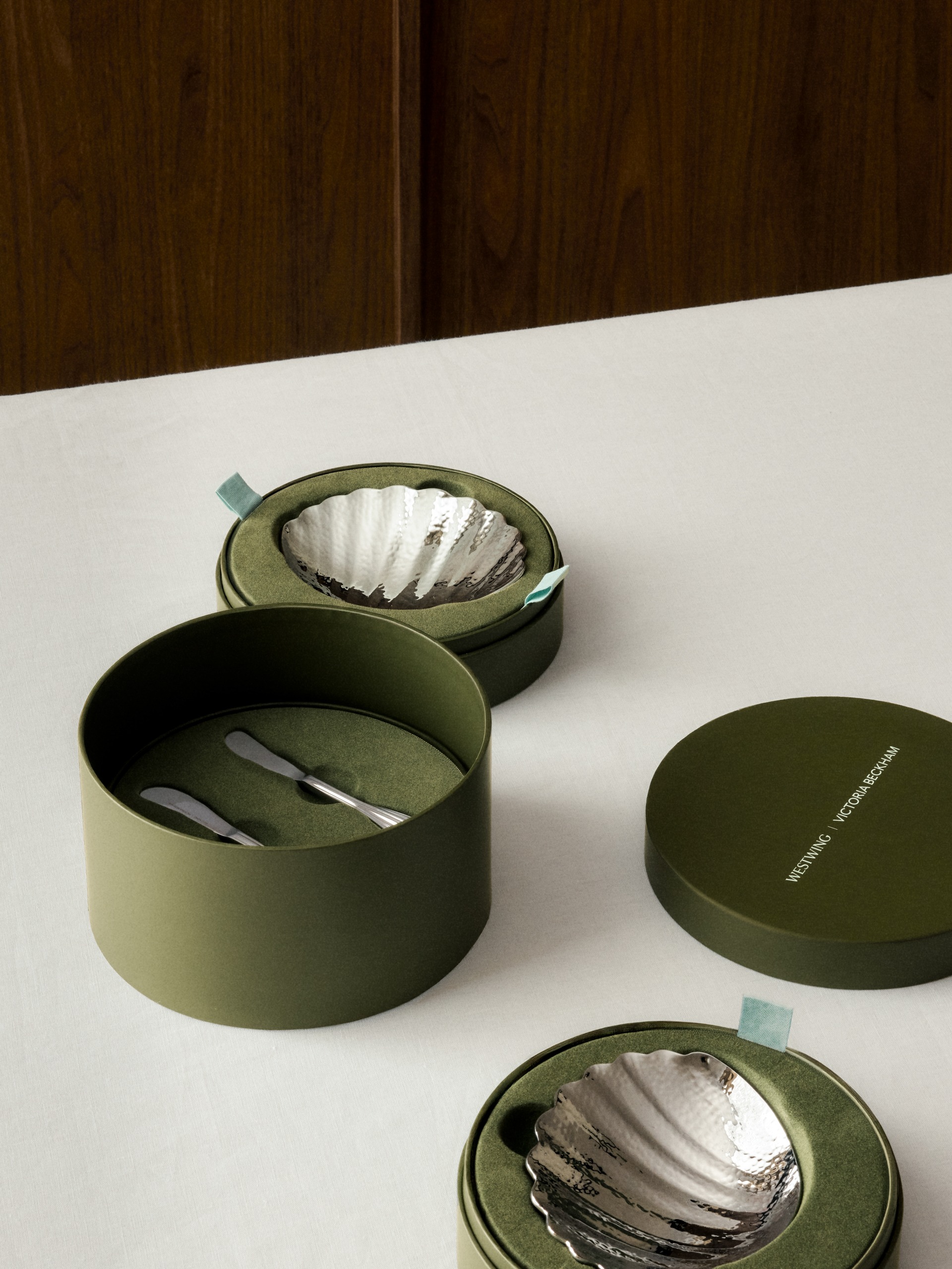 white tablecloth with timber wall, with round green box with chrome shell-shaped butter dish in it