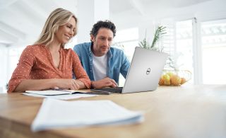 A smiling man and woman sitting at a table using a Dell laptop together.