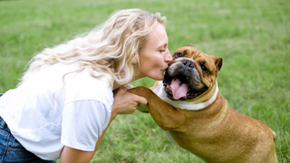 Blonde woman kissing a bulldog breed in the park with his front legs in her hands