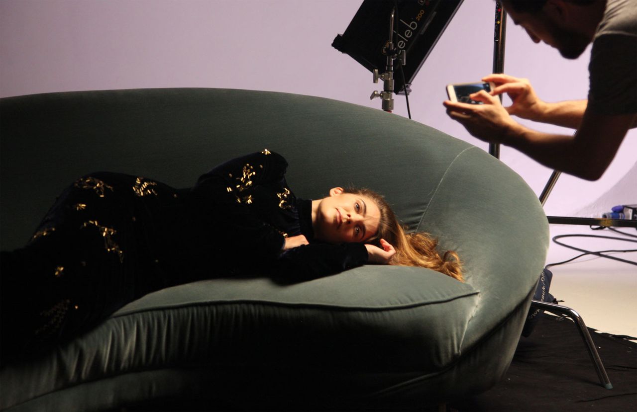 Joanne Salley lying on a green sofa in a black dress for a photographer 