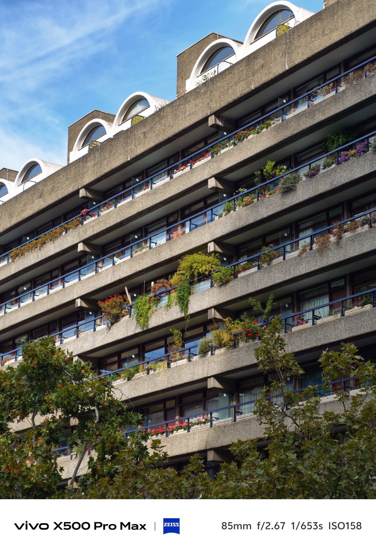 Brutalist apartment building with long balconies covered in plants and flowers.