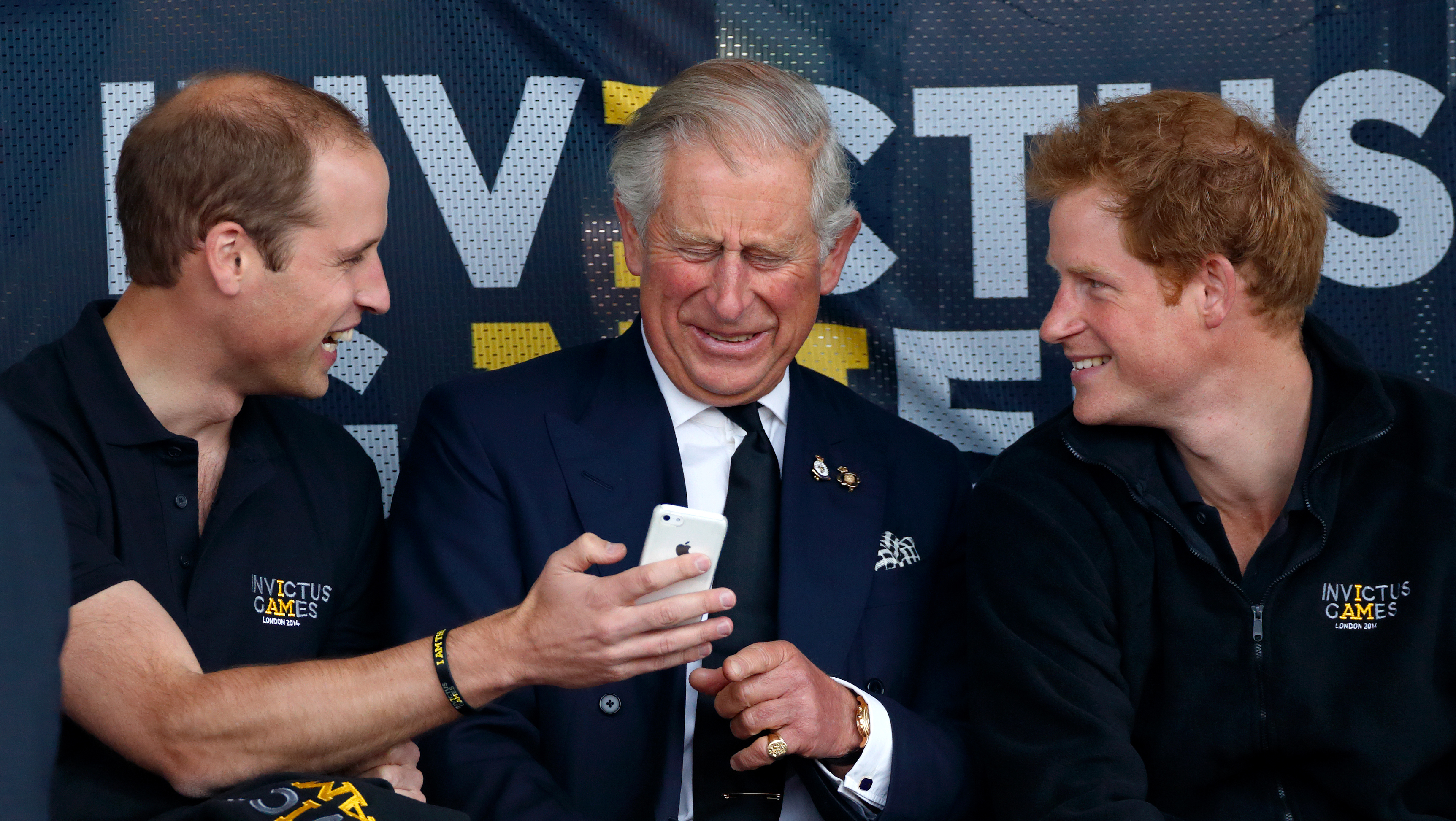 Prince WIlliam showing his phone to King Charles and Prince Harry while they laugh