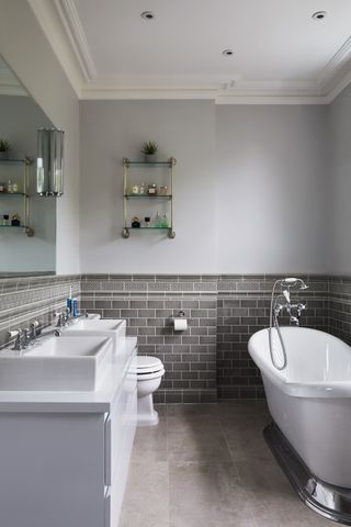 A traditional style bathroom with slipper bath, two basins and dark grey tiling. Home of Sue and Matt, a renovated Victorian house in London.