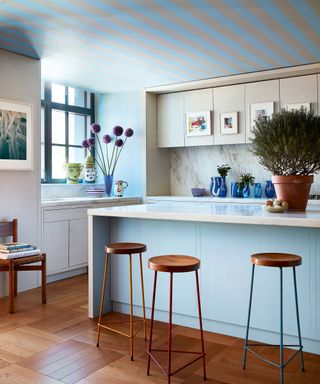 kitchen with blue island, white cabinets, striped ceiling and wooden barstools