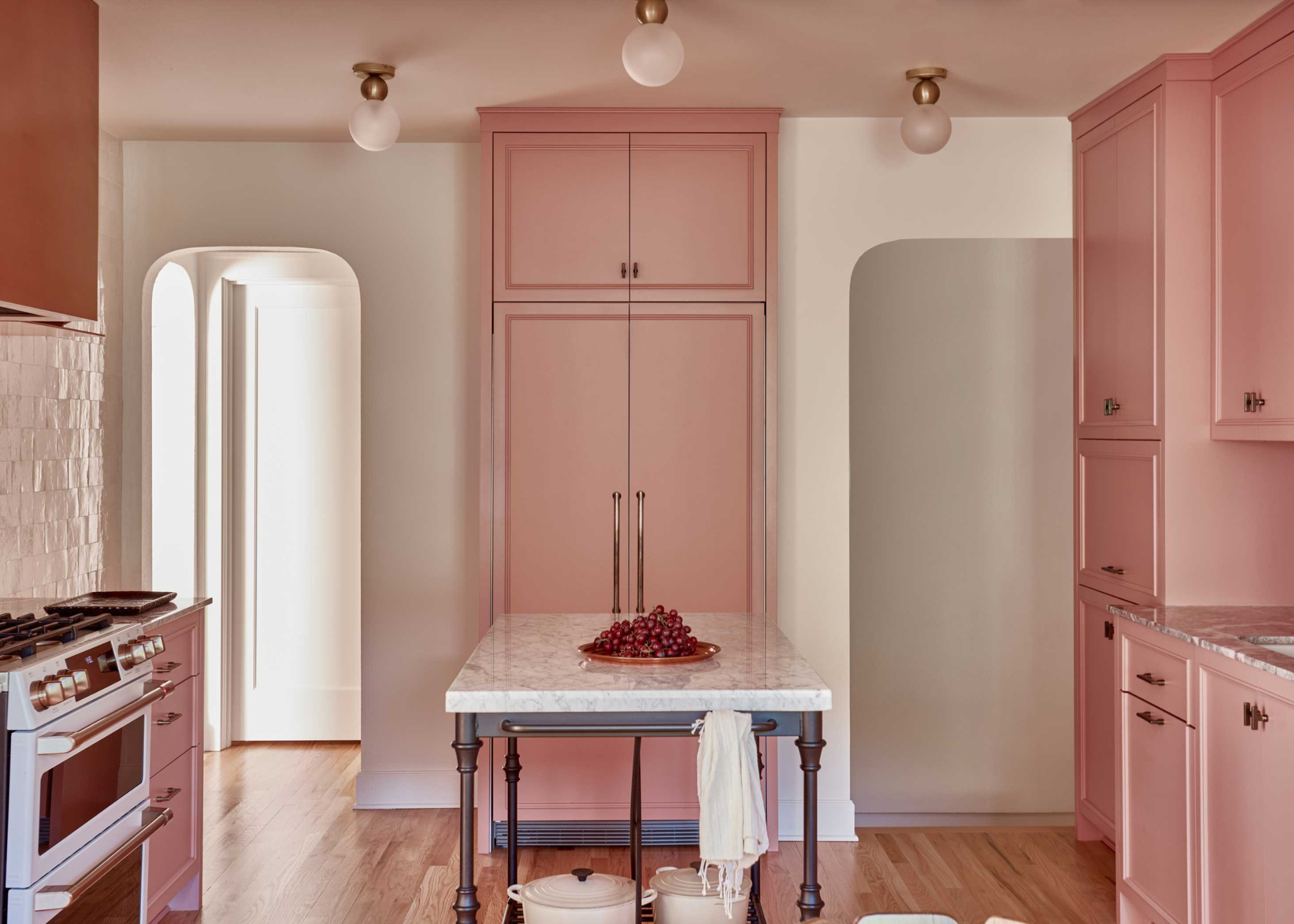 pink built-in kitchen cabinetry that goes right the way up to the ceiling with rounded open doorways and a portable island in the centre