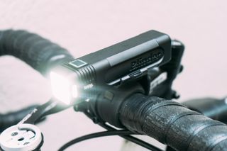 A black bike light mounted on top of a set of handlebars and turned on