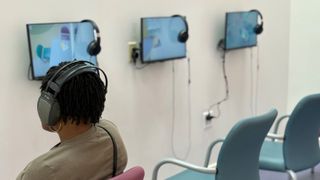 A woman sits with headphones on watching a monitor. 