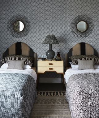 Twin single beds with gray and white bedding and two round mirrors above