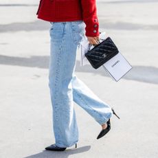 A woman wearing jeans, crossing the road, holding a beauty hall perfume, Chanel carrier bag 