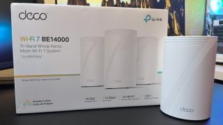 A photo of a TP-Link Deco BE68 mesh router stood next to its retail packaging.