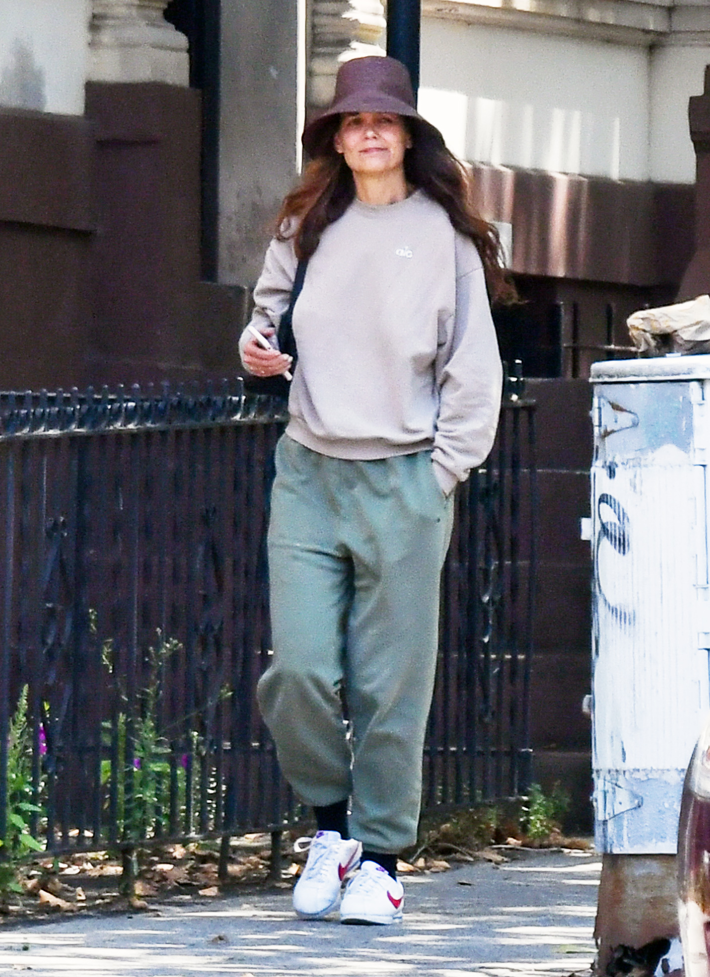 Katie Holmes wears Nike sneakers, green sweat pants, a sweatshirt, and a bucket hat