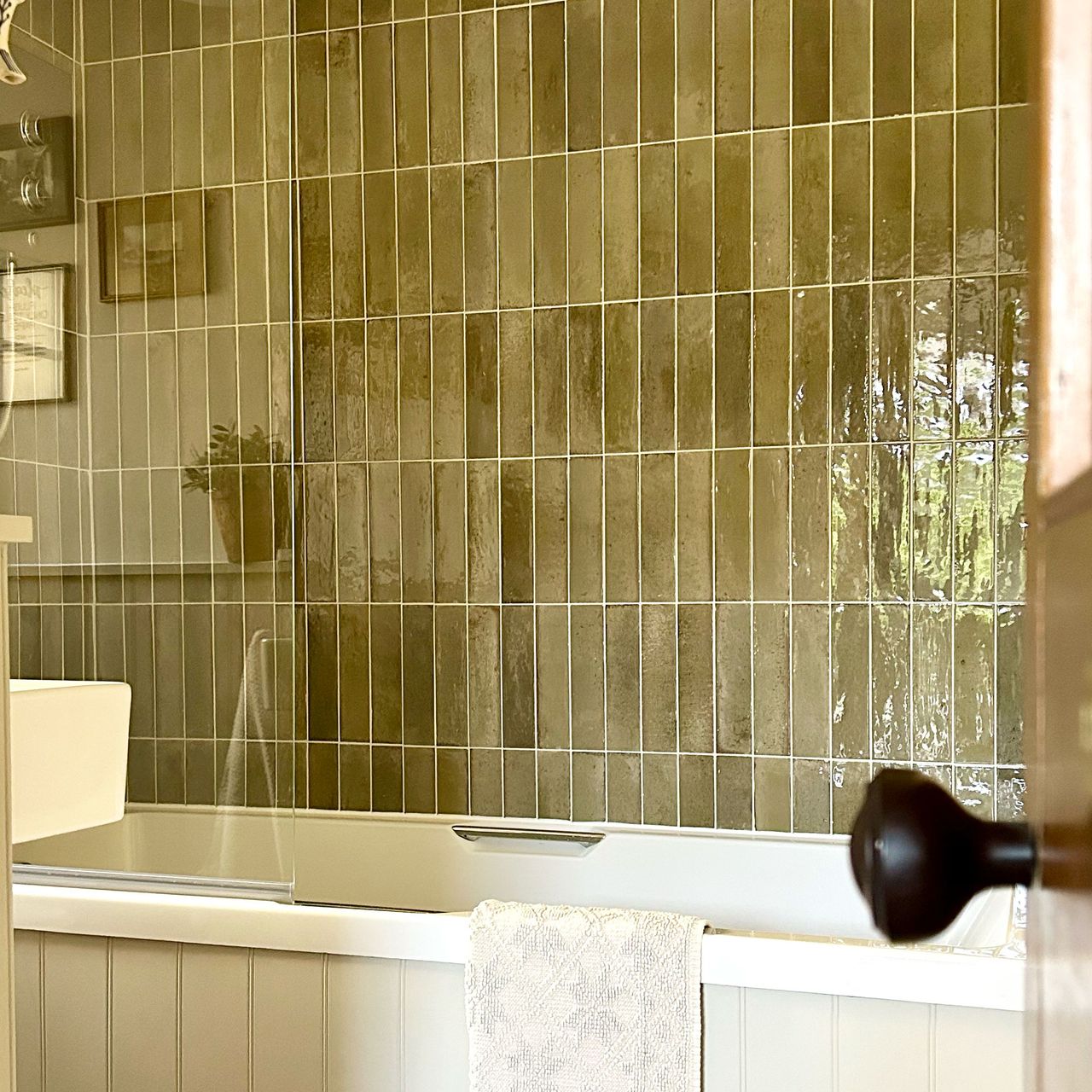 Cream panelled bath surrounded by green rectangular wall tiles