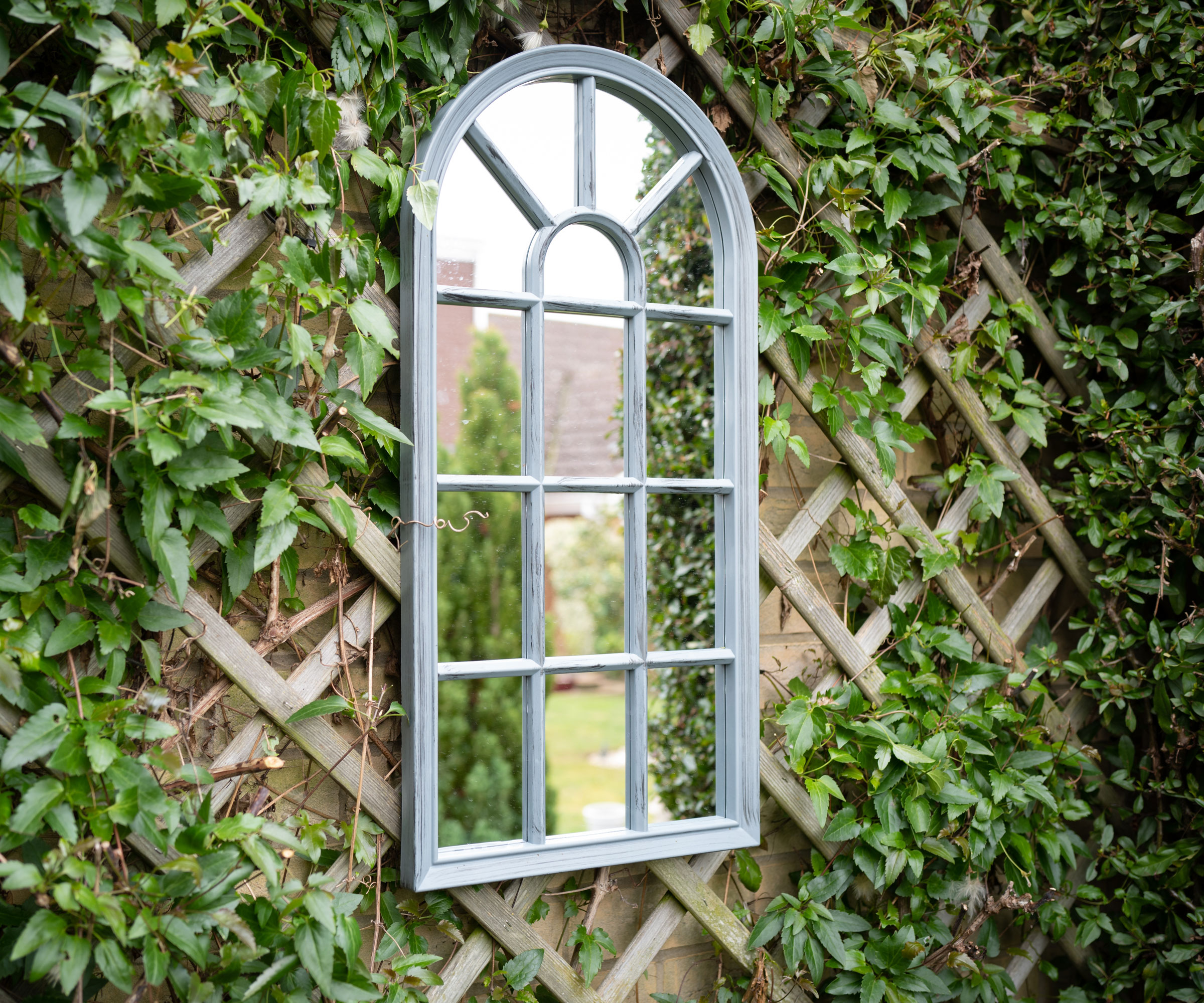 arched garden mirror against wall with trellis and climbing plants