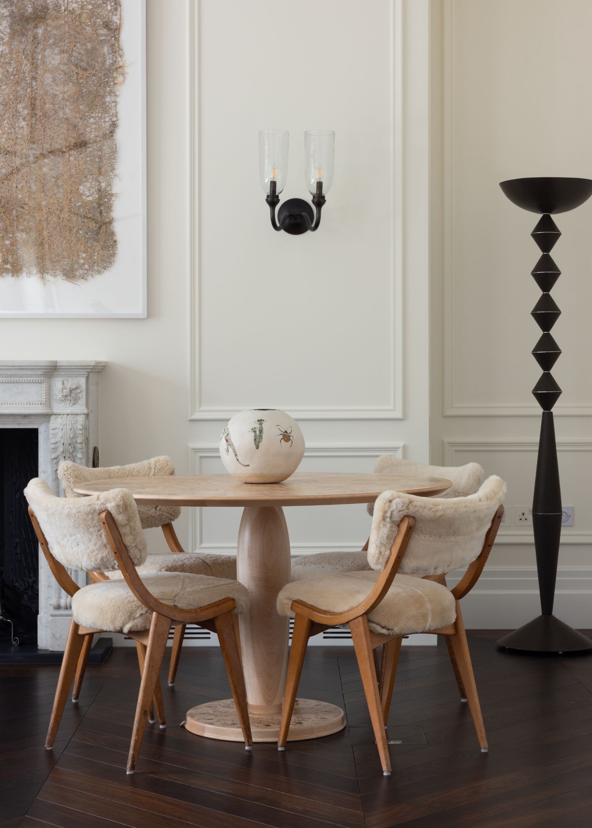 A Victorian living room with cream paneled walls, a fireplace in the corner and dark wood flooring, and a round table with four dining chairs.