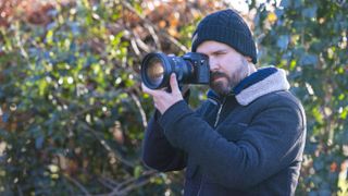 Professional photographer Dan Mold shooting with a Sony A7R IV and Sigma 135mm f/1.4 DG | Art lens brought up to his eye shooting through the viewfinder outdoors